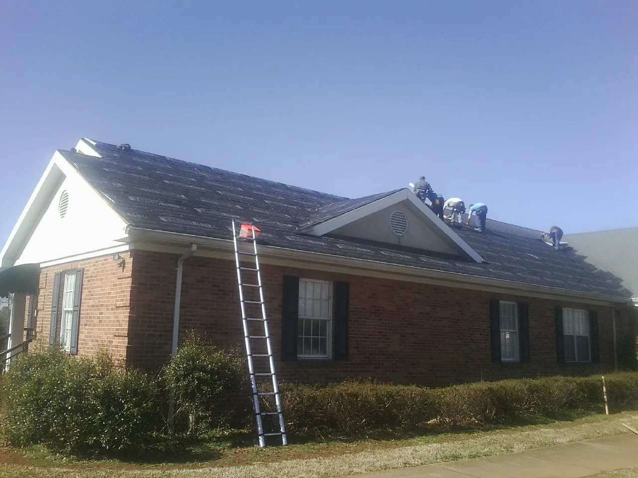 Crew tearing shingles off a brick ranch roof with a ladder set — Metal Roof Repair work by our crew in Farwell