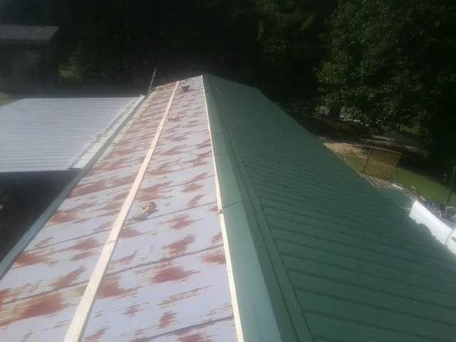 Old rusted panels beside newly installed green metal roofing — Wind Damage Roof Repair by Roofing Brothers in Farwell