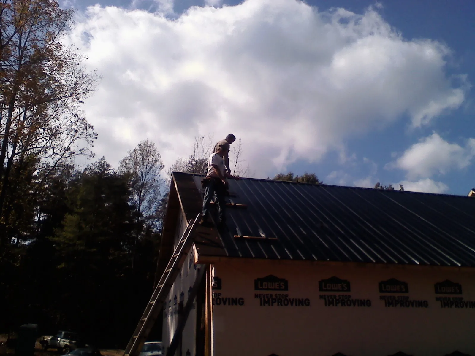 Roofer fastening dark metal panels high against a cloudy sky, from a Roof Inspection job in Farwell